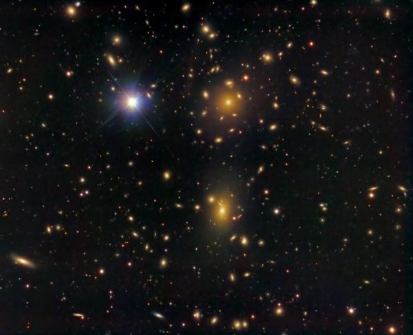 The Coma cluster of galaxies, whose galaxies move far too quickly to be accounted for by gravitation given the mass observed alone. Image credit: KuriousG of Wikimedia Commons, under a c.c.a.-s.a.-4.0 license.